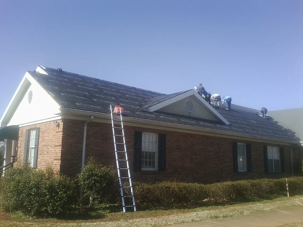 Crew tearing shingles off a brick ranch roof with a ladder set — Metal Roof Repair work by our crew in Cresco