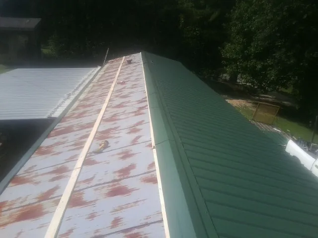 Old rusted panels beside newly installed green metal roofing — Wind Damage Roof Repair by Roofing Brothers in Cresco