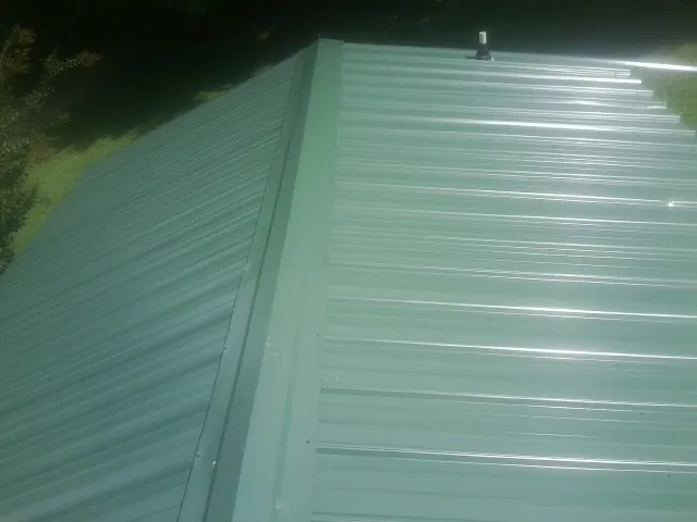 New green metal panels meeting at the ridge of a roof — Flat Roof Repair work by our crew in Cresco