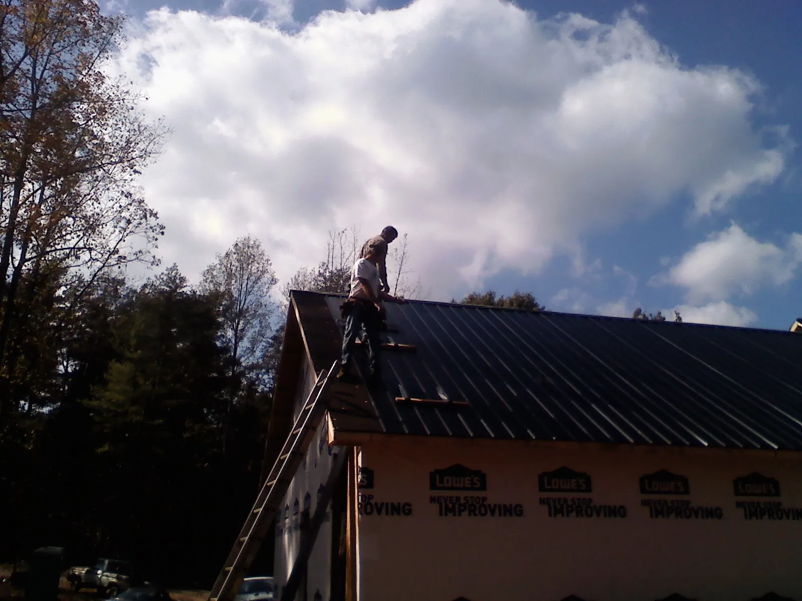 Roofer fastening dark metal panels high against a cloudy sky, from a Roof Inspection job in Cresco