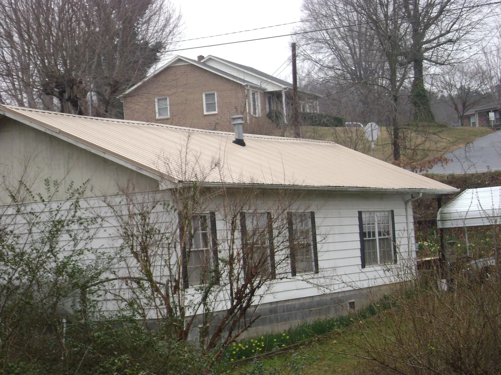 Tan metal roof on a white sided house set into a hillside — Commercial Roofing by Roofing Brothers in Cresco