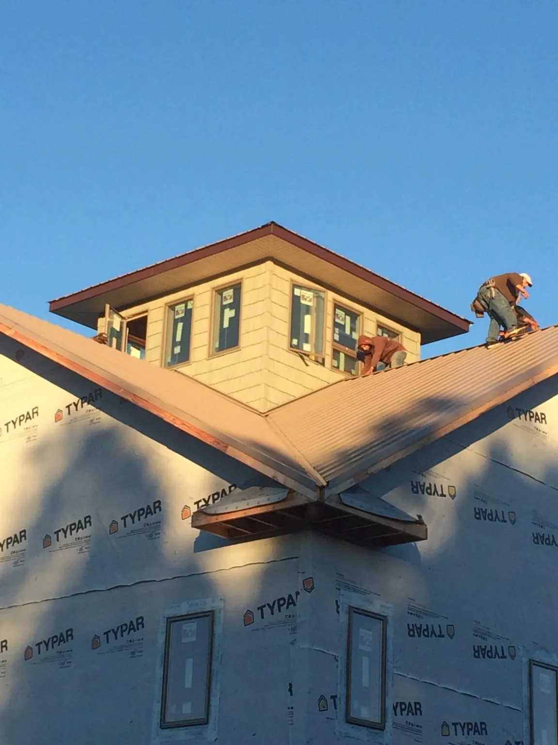 Roofers working around a rooftop cupola on a new metal roof at sunset — Roof Waterproofing in Cresco by Roofing Brothers